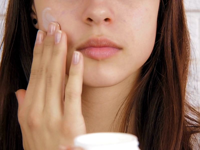 devojka nanosi kremu na lice